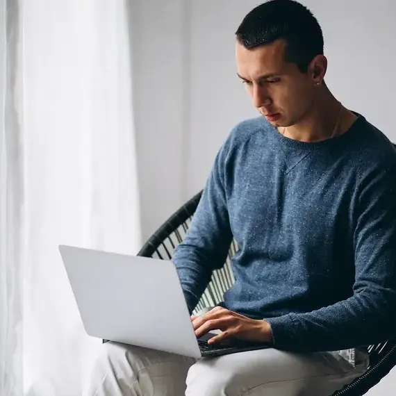 Desenvolvedor focado trabalhando em um laptop prata, sentado em uma cadeira de design em ambiente iluminado.