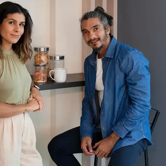 Homem e mulher, consultores da LCM Sistemas, sorrindo em um ambiente de escritório moderno com prateleiras de madeira ao fundo.